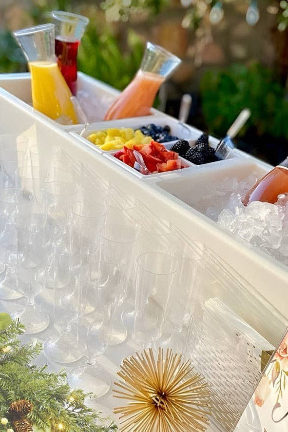 Bottles of champagne on ice with colorful drinks and snacks in the background.