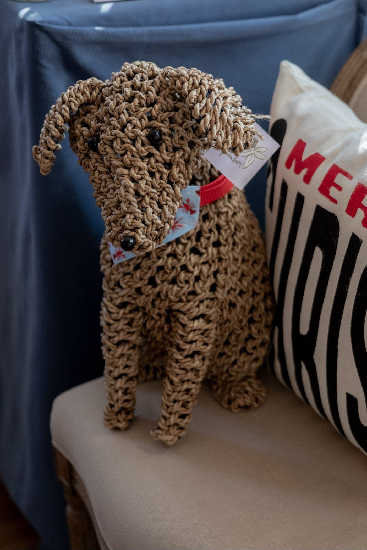 Knitted dog toy with a tag on a chair next to a striped pillow