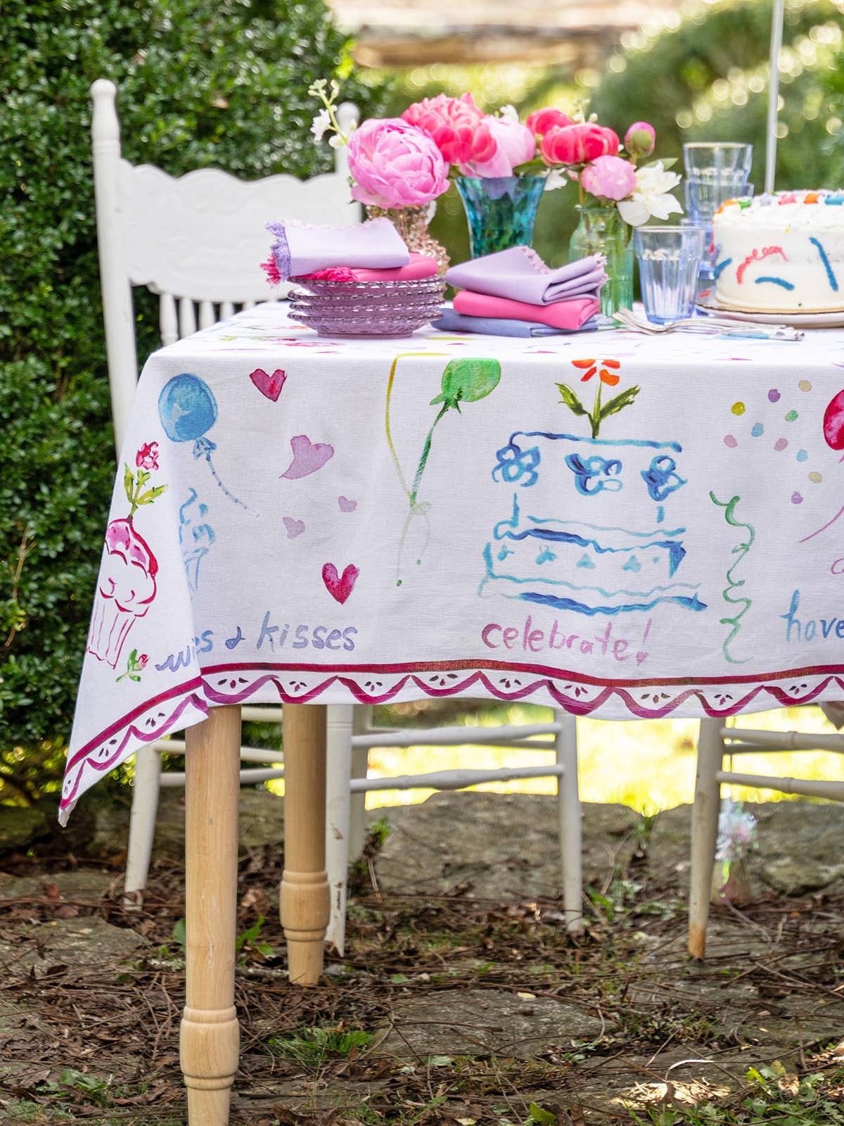 Decorated table with a children's tablecloth, flowers, and a cake outdoors.
